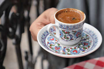 hand holding a a cup of turkish coffee on table 
