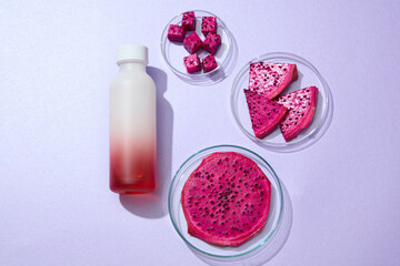 Top view of a glass bottle decorated with fresh slices of red dragon fruit on purple background. The high vitamin B3 content in dragon fruit soothes sunburned skin and reduce inflammation