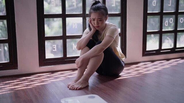 Young Asian woman holding her head  frustrated over gaining weight at home weight control.