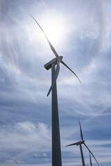 Clean green energy generation, closeup of wind turbines on a wind farm with sun halo in background
