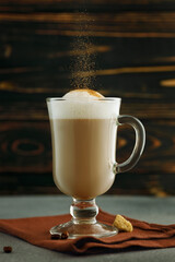 cappuccino in glass cup with falling cinnamon powder on table