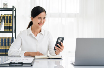 Happy senior woman using mobile phone while working at home with laptop. Smiling mature woman messaging with smartphone. Beautiful stylish elderly lady browsing site on cellphone.