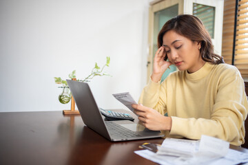 A woman uses a calculator to check the sum of her home expenses and she is stressed over the home expenses.