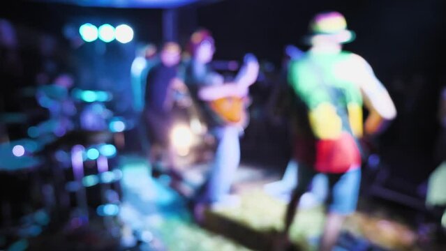 Blurred video of rock band members performing on stage. Guitarists and keyboardist playing on an outdoor stage in the light of multi-coloured spotlights