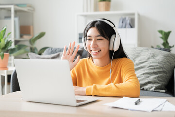 Happy Asian girl waving in greeting friend on laptop at home with earphones
- 647052211