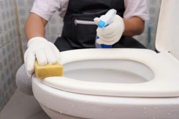 Close up of male wearing gloves and apron brushing the dirty toilets in the bathroom