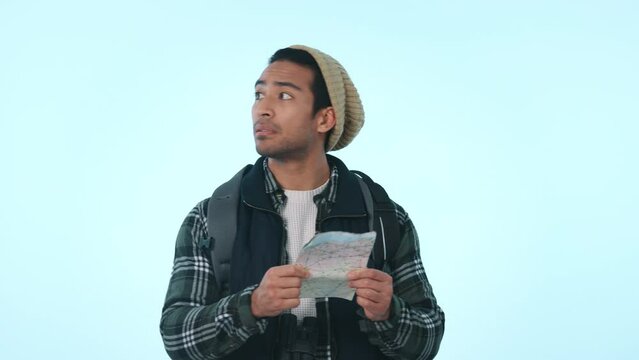 Travel, lost and confused with man and map in studio for location, hiking and tourism. Adventure, search and vacation with person and paper on blue background for direction, journey and holiday