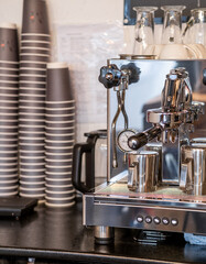 The barista prepares fresh coffee in the coffee machine in the morning in the cafe. There are coffee cups on the table for customers. Coffee machine close-up