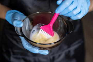 girl in blue rubber protective gloves holding a brush in her hands and stirring hair dye close-up colorist hair care at home hair mask.  - Powered by Adobe