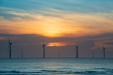 Fans of wind turbines spin over the sparkling sea. Dynamic clouds at sunset. An offshore wind farm off the northwest coast of Taiwan. One of green power.
