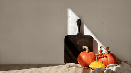 Orange pumpkins, wooden board, and linen tablecloth on beige table. Minimal kitchen autumn interior...