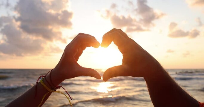 Heart from hands of couple on beach at sunset. Honeymoon and romantic encounter