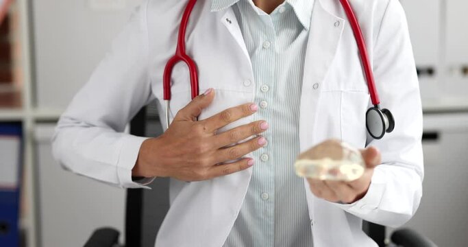 Doctor plastic surgeon holds silicone breast implant and thumbs up. Recommendation of quality breast implants