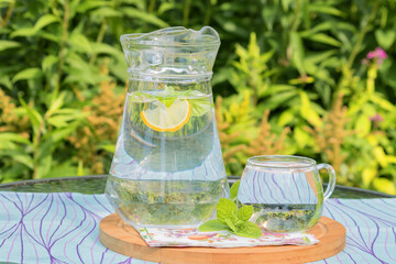 On the garden table in a glass jug herbal drink with mint and lemon.