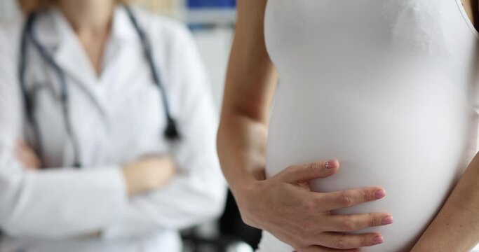 Pregnant woman strokes big belly and an obstetrician-gynecologist in clinic. Patient consultations in clinic room