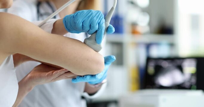 Doctor makes ultrasound of the patient elbow joint in clinic closeup. Orthopedist and elbow pain causes and diagnosis