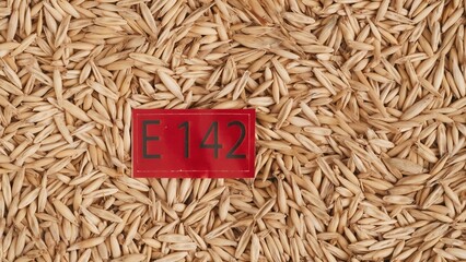Closeup shot of wheat grains background and red paper with E 142 written on it.