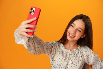 Teen girl making a selfie on her phone against yellow background