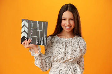 Happy smiling girl portrait holding clapper board on yellow background