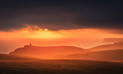 Dramatic skies and sunset behind Belle Tout lighthouse from the cliff edge of Beachy Head on the south downs east Sussex coast south east England UK
