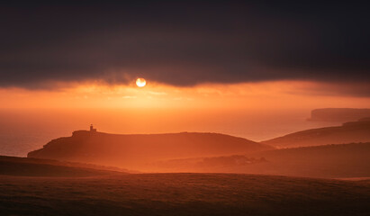 Dramatic skies and sunset behind Belle Tout lighthouse from the cliff edge of Beachy Head on the south downs east Sussex coast south east England UK