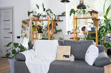 Key to home with keychain and mock up frame miniature of house on gray sofa in white interior with potted plants. Design, project, moving to new house, mortgage, rent and purchase real estate