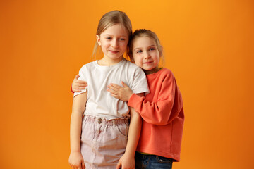 Two cute little girls standing on yellow background in the studio