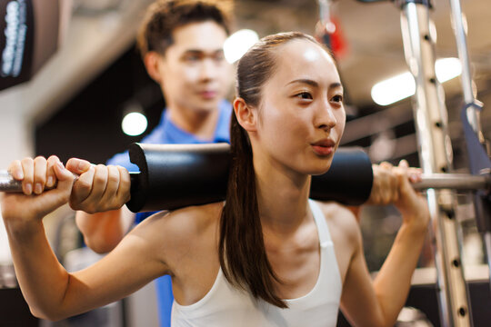 パーソナルトレーナーの導きでマルチトレーナーマシンで運動する若いアジアの女性