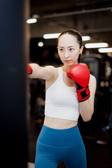 ボクシンググローブとパンチングバッグでトレーニングする若いアジアの女性 - obrazy, fototapety, plakaty