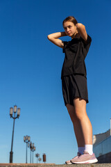 Young, fit and sporty girl in black clothes stretching after the workout in the urban city park.