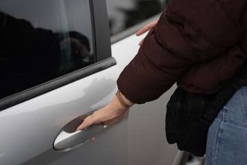 Primer plano de una chica con una campera puffer marrón abriendo la puerta de su coche gris - obrazy, fototapety, plakaty