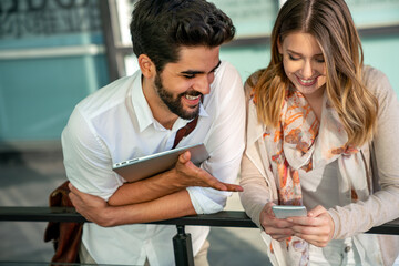 Obraz premium Happy young business people chatting and using digital devices together outdoors