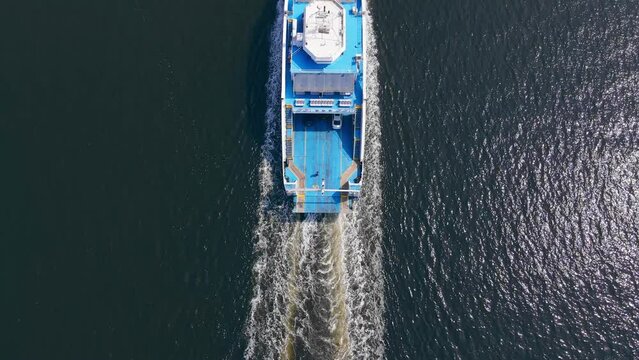 Vehicle ferry boat with water trail transporting cars across sea strait, aerial view
