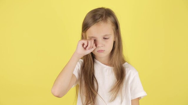 Kids problems. Studio portrait of upset child girl crying and wiping her tears, yellow background.