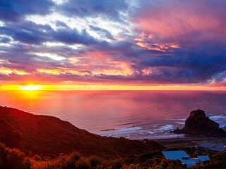 Sunset with dramatic clouds over Tasman sea at Piha beach. View of Lion rock. Auckland, New Zealand