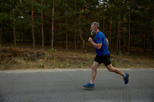 Side view motion shot of retired senior sportsman running among road
