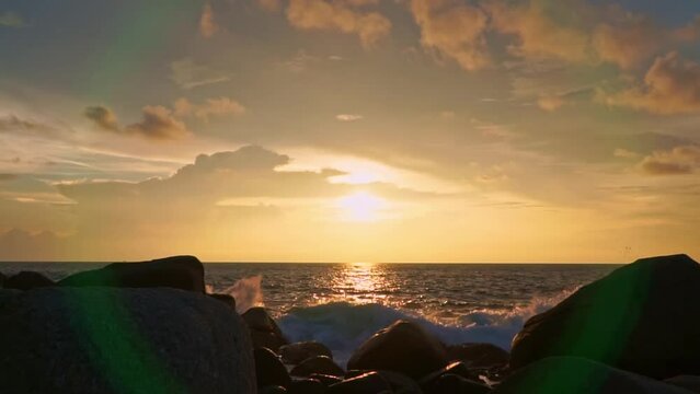 .slow motion scene of waves hitting the rocks at bright yellow sunset..Waves lapping on the rocky beach in the stunning sunset..slowly waves lapping on the rocky beach in a white foam wave..