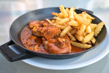 Pork steak with mushroom sauce and fries served in an iron pan, meal with meat for lunch or dinner, selected focus