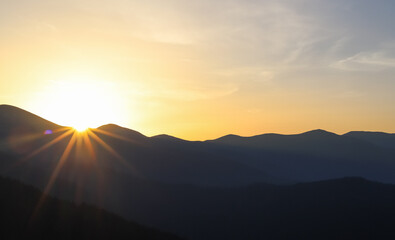 dawn in the mountains, the sun appears over the black silhouettes of mountain peaks