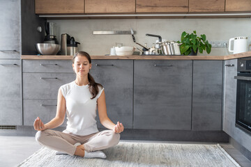 Young woman is sitting and doing meditation on background of dirty dishes in the kitchen. Slowdown,...