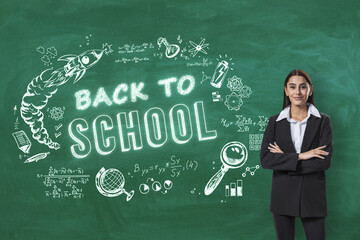 Attractive young business woman with folded arms standing on creative back to school sketch on blackboard background. Education, knowledge, and wisdom concept.