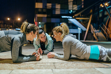 Young women friends sport team having fun while doing plank exercise during training together on the empty city at night