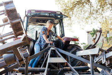 Female worker checking tractor on farmland at daytime