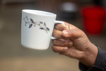 A human hand holds an old tea cup and the background blur