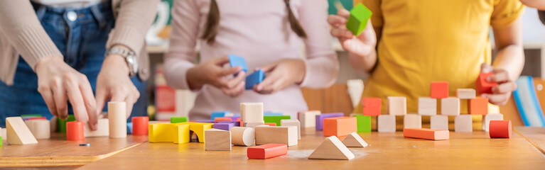close up hands of little children playing blocks in classroom. Learning by playing education group study concept. International pupils do activities brain training in primary school background banner - obrazy, fototapety, plakaty