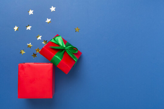 Open red gift box with party confetti on color background, top view