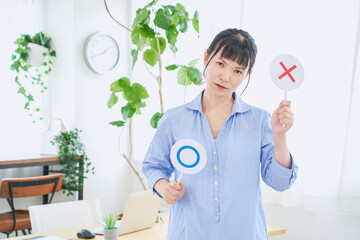 マルバツの棒を持つ自宅で仕事をする女性　立ちポーズ