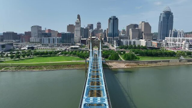 John A. Roebling Suspension Bridge in downtown Cincinnati, Ohio over the Ohio River. Aerial establishing shot on beautiful summer day with city skyline in the distance.
