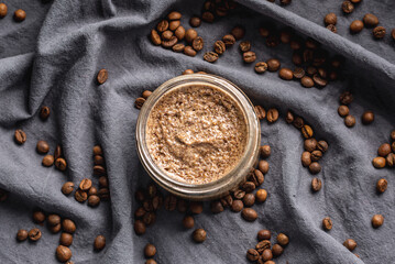 Organic oil scrub with sugar and coffee on the background of coffee beans on black cloth. Concept of natural cosmetics and skin care