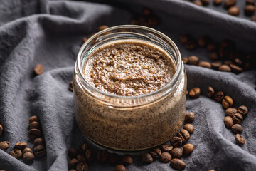 Obraz na płótnie Canvas Natural coffee scrub in a transparent glass jar on the background of coffee beans on a black cloth. Concept of organic cosmetics and skin care